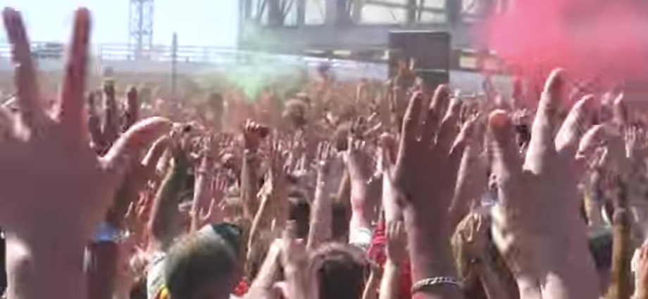 mani di una multitudine di persone alzate verso il cielo; fumogini rosa.